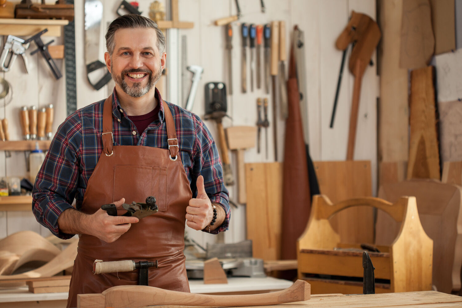 Maestro carpintero sonriendo en su taller, rodeado de herramientas y piezas de madera